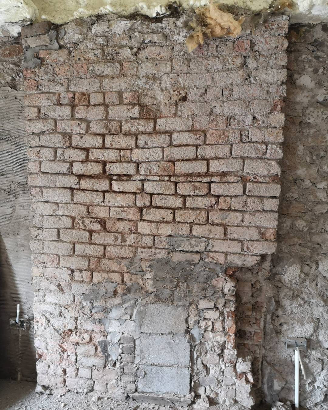 An exposed brick chimney breast running the height of a stripped wall.