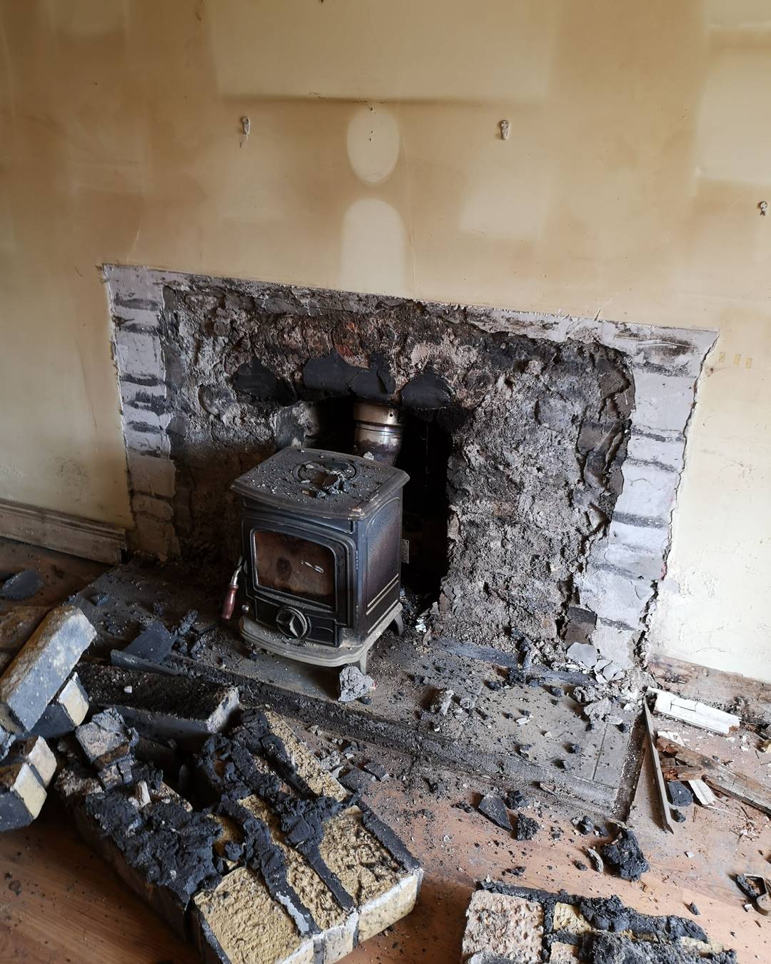 A stove pulled clear of a gutted chimney breast, rubble across the floor.